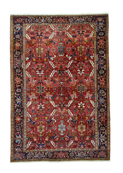 A rectangular traditional oriental rug with a deep red field, intricate floral motifs, and a dark navy blue border with beige and gold details, shown flat against a white background.
