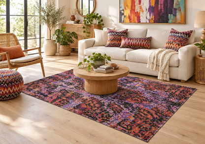 A colorful area rug with a distressed, distressed-style bohemian pattern in purple, red, orange, and black, styled in a bright modern living room with a white sofa and wooden coffee table.