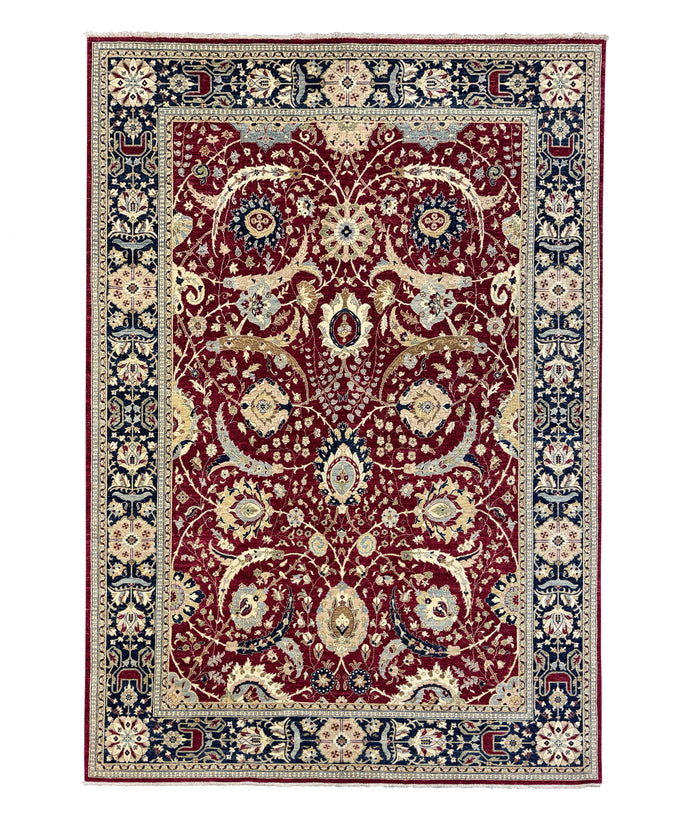A traditional oriental-style area rug with an intricate floral and vine pattern, featuring a deep red central field, navy blue borders, and cream accents.
